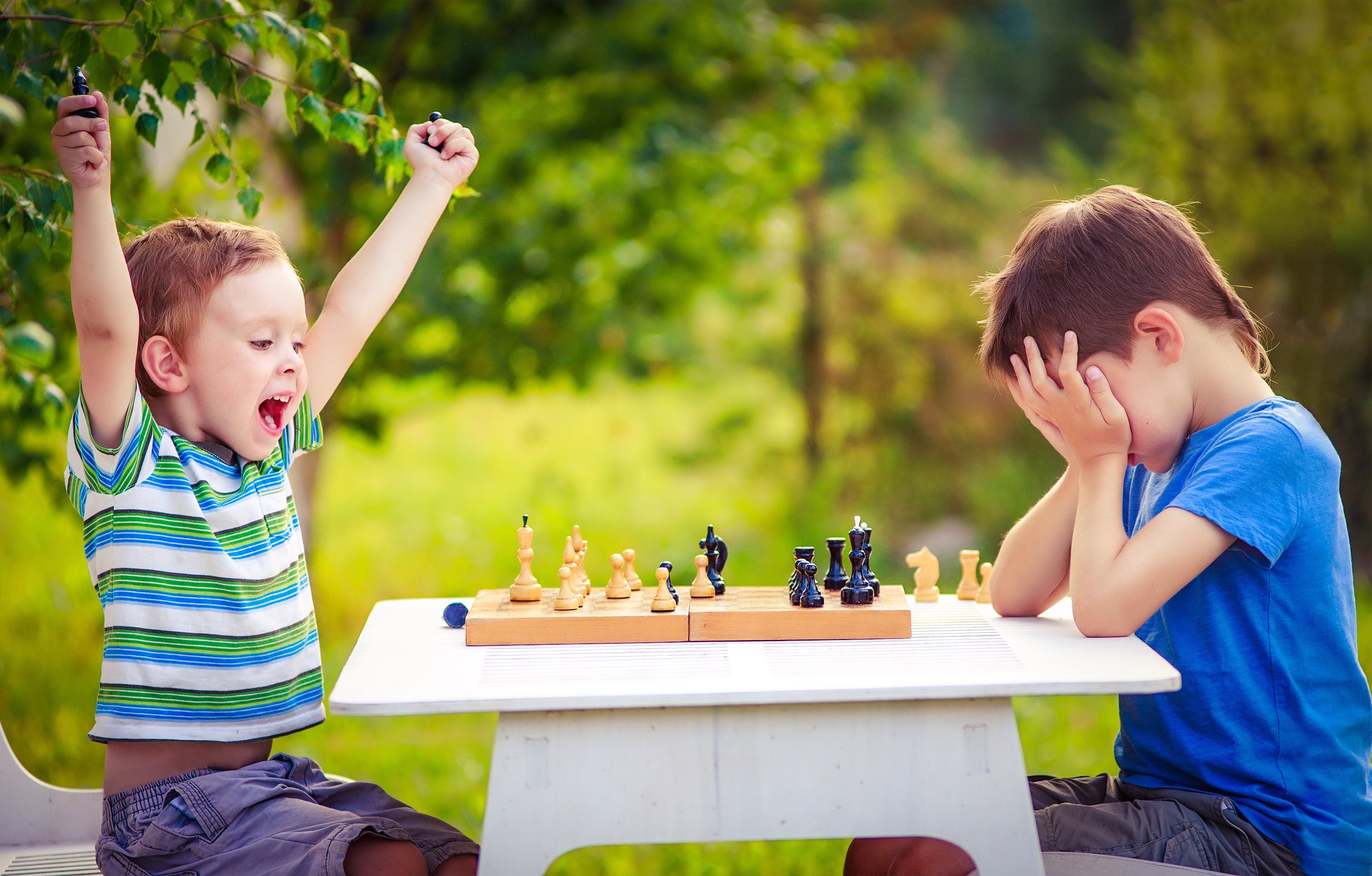 vivid emotions after the game of chess. two young chess players outdoors. boy rejoices won a game of chess. sad opponent covered his face, and upset losing