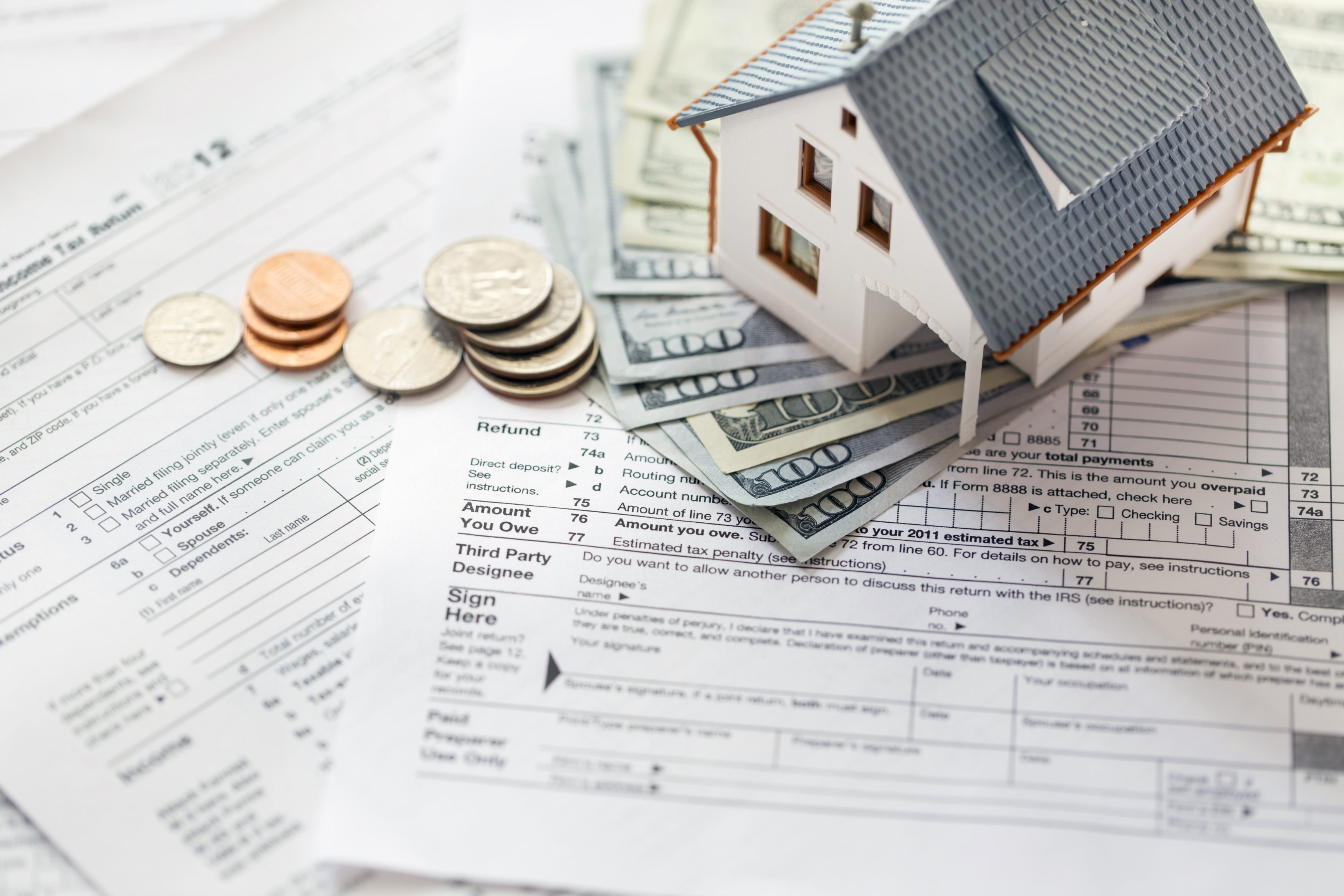 Miniature house with money on tax papers