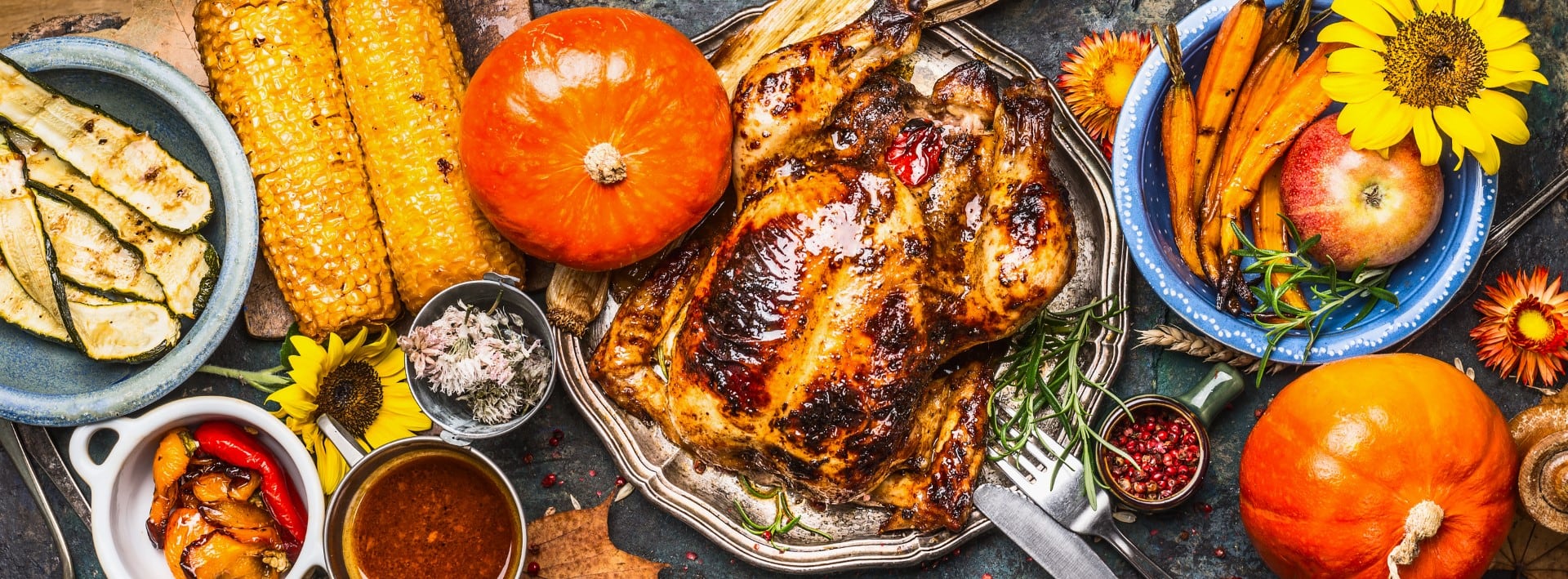 Thanksgiving Day food. Various grilled vegetables ,roasted chicken or turkey and pumpkin with sunflowers decoration on dark background, top view, banner