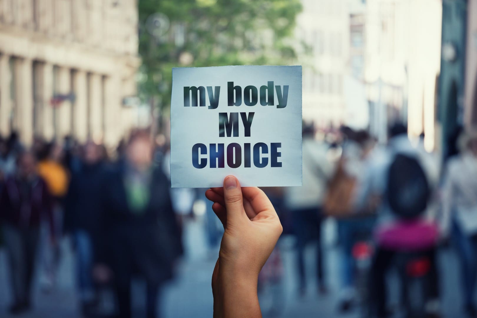 Feminist hands holding a protest banner with the message my body my choice over a crowded street. Human rights concept against fetus law and reproductive justice. Stop discrimination and injustice