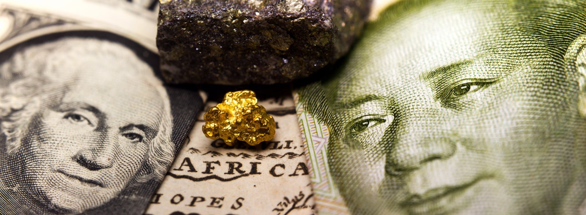 Close-up of a gold nugget / rare earth metal in between a 1 dollar note (showing George Washington) and Mao on a 1 yuan Chinese banknote  on top of an old map of Africa