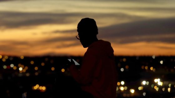 FILE - In this March 25, 2020, file photo, a person looks at a phone as the sun sets, in Kansas City, Mo. The city along with neighboring counties is under Stay at Home orders to help prevent the spread of COVID-19, the disease caused by the new coronavirus. (AP Photo/Charlie Riedel, File)
