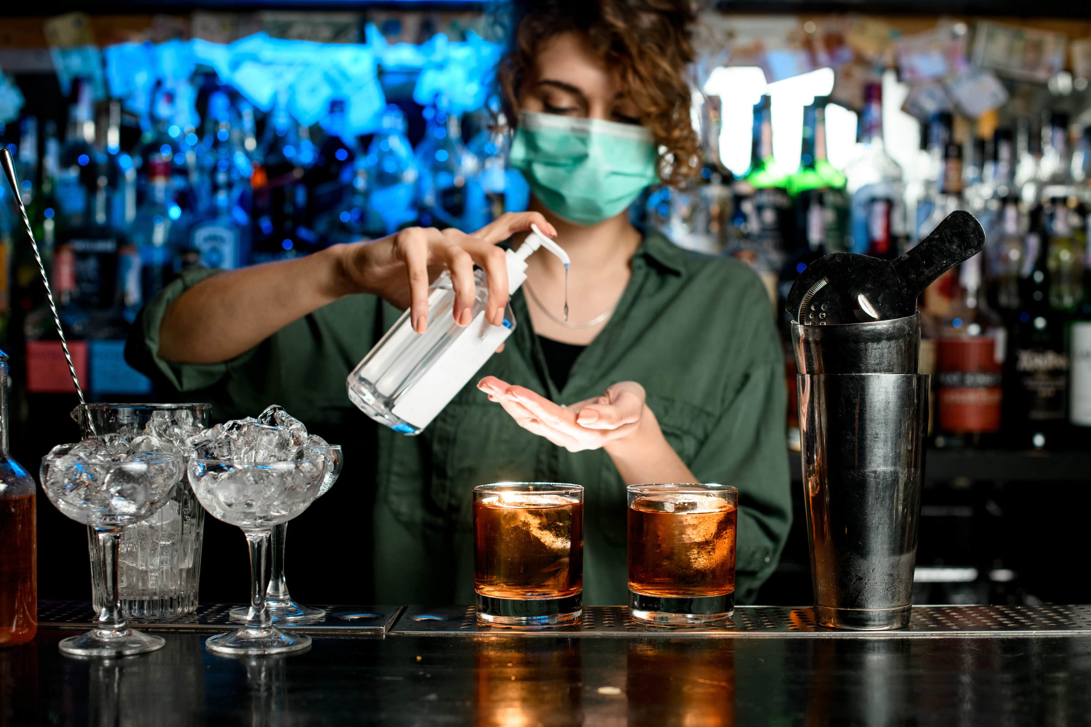 Woman bartender in medical mask treats her hands with disinfector bar