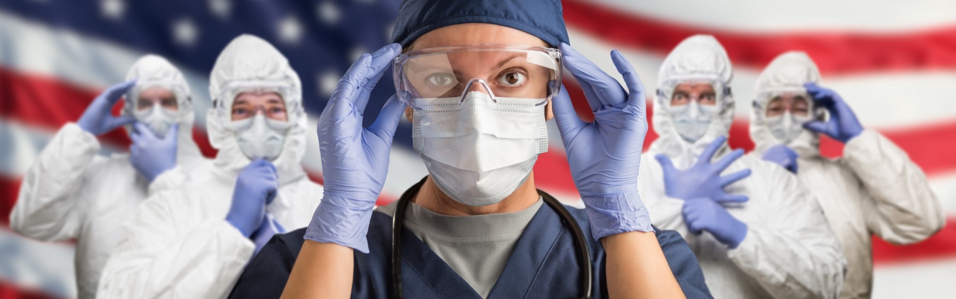 Doctors or Nurses Wearing Medical Personal Protective Equipment (PPE) Against The American Flag Banner.