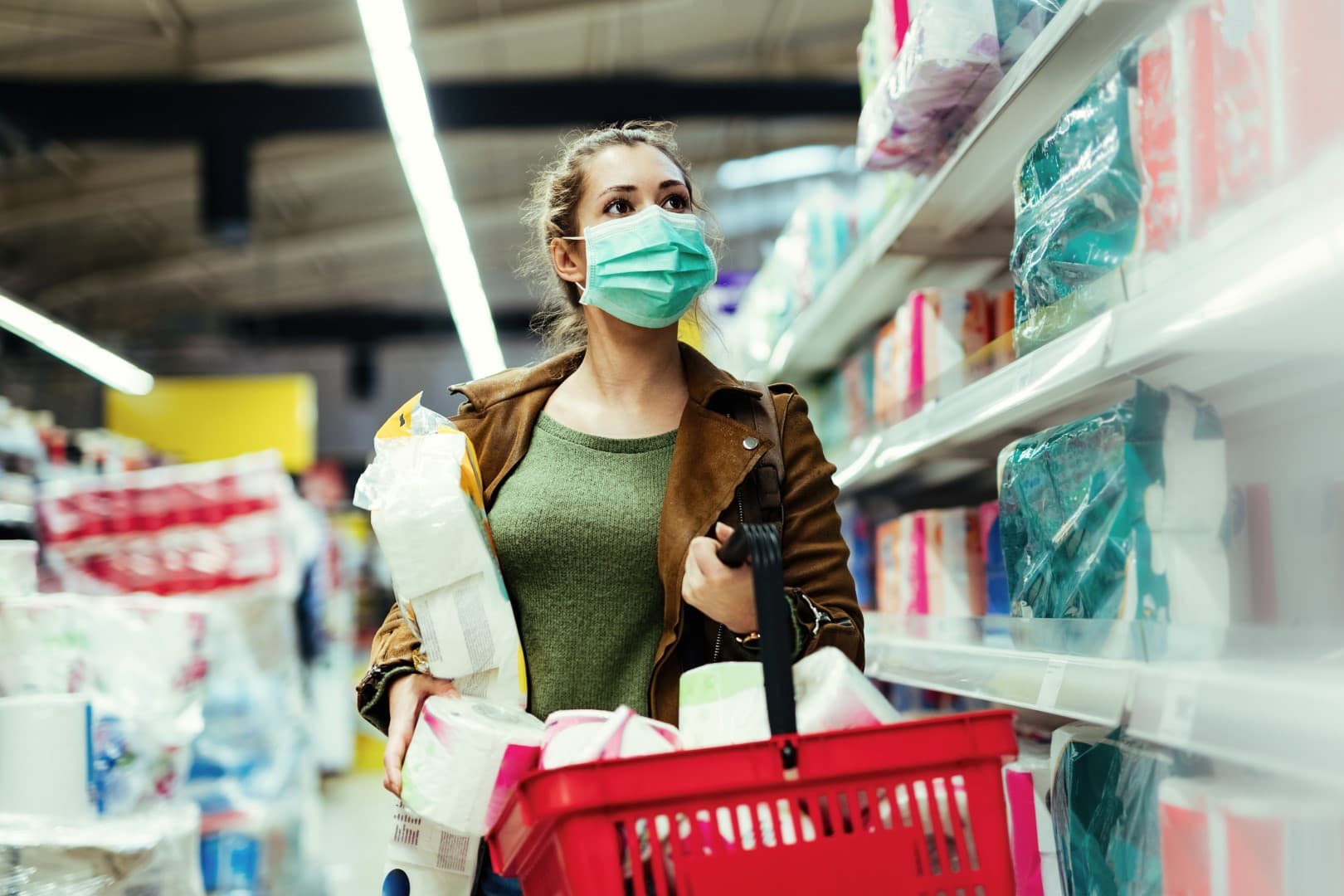 Woman with protective face mask buying toilet paper in the store during virus epidemic.