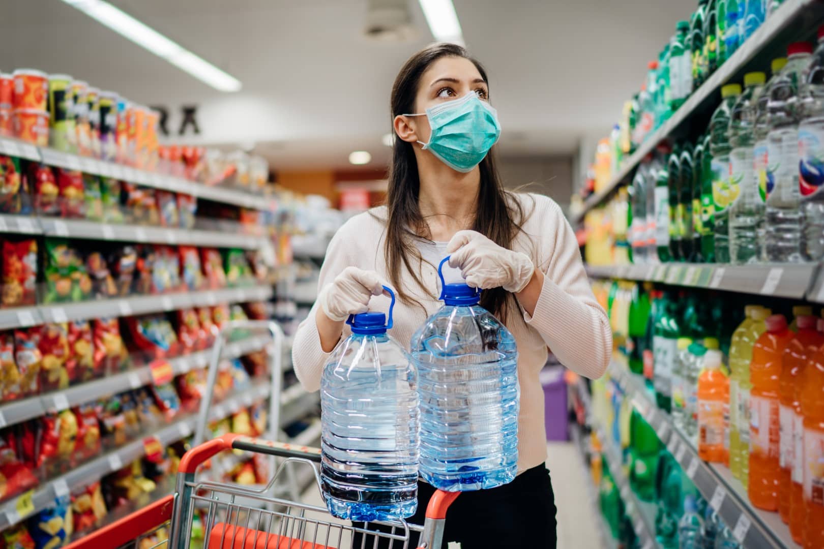 Woman wearing face mask buying bottled water in supermarket/drugstore with sold-out supplies.Prepper buying bulk supplies due to Covid-19 or Coronavirus and panic buying concept.