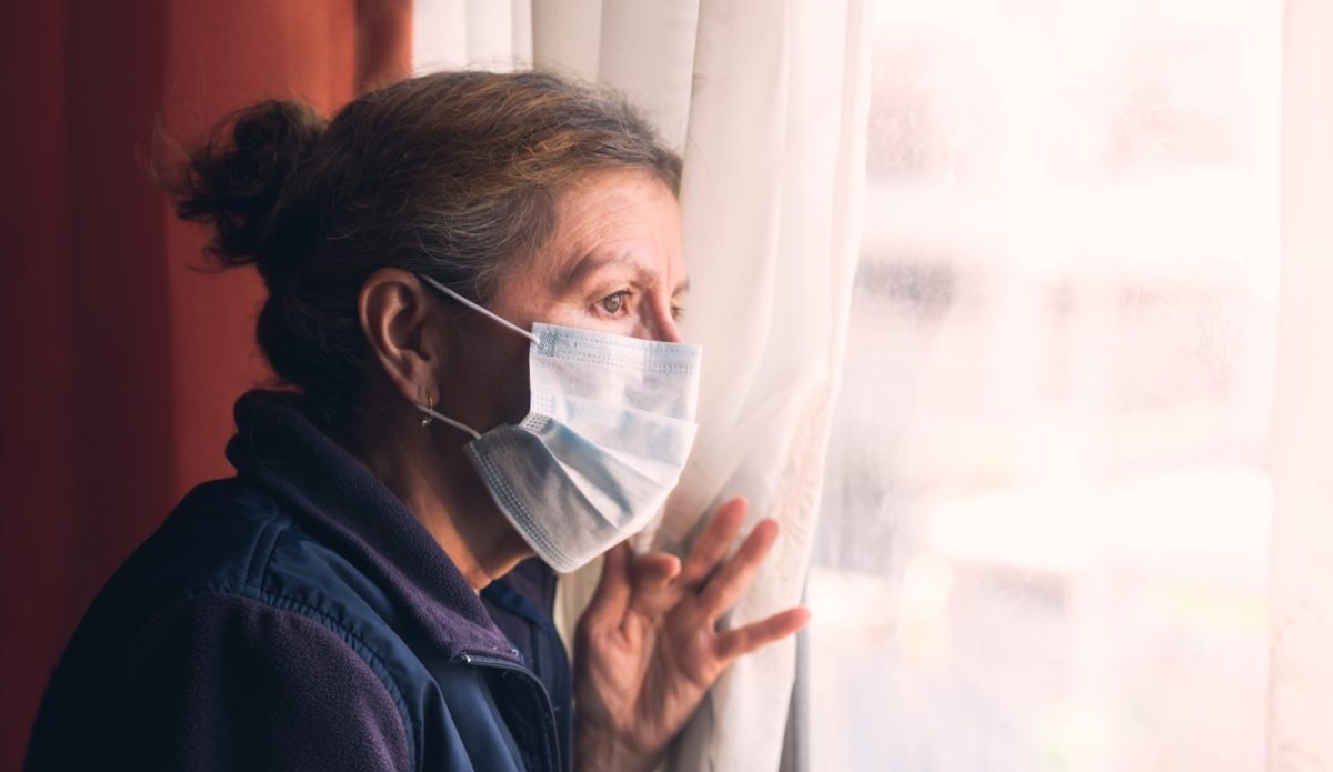 Coronavirus. Sick grandma of corona virus looking through the window and wearing mask protection and recovery from the illness in home. Quarantine.