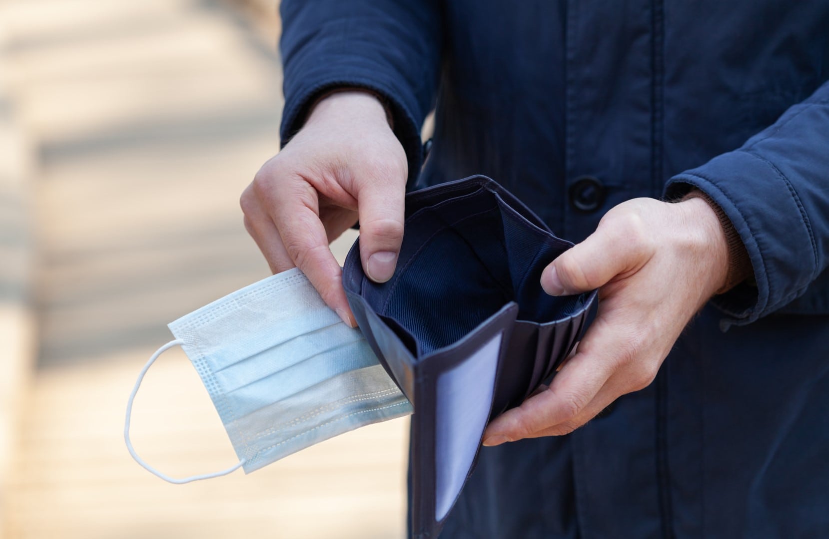 Man holds a medical mask and empty wallet without money. Bankruptcy and unemployment resulting from the global coronavirus epidemic.