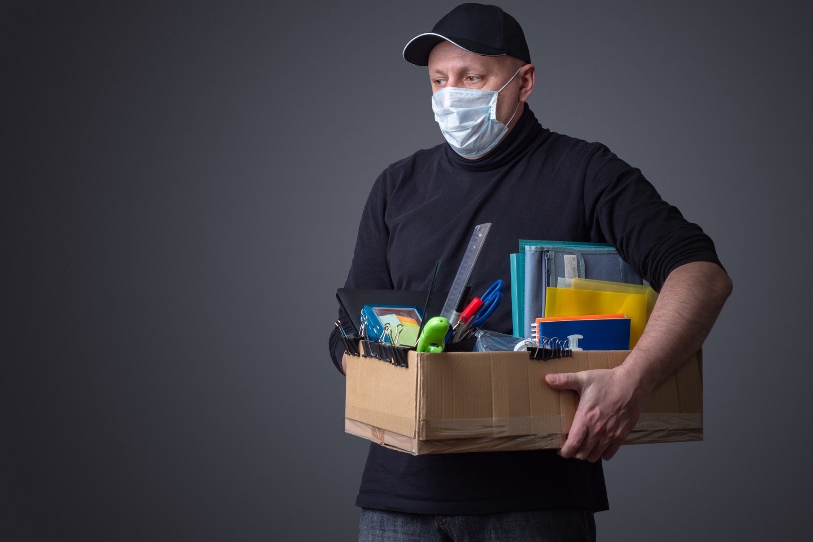 A sad man in a mask with a box of office supplies in his hands. The loss of a job because of the epidemic of the coronavirus. Unemployment. Bankruptcy of enterprises. Ruin of entrepreneurs. Crisis.