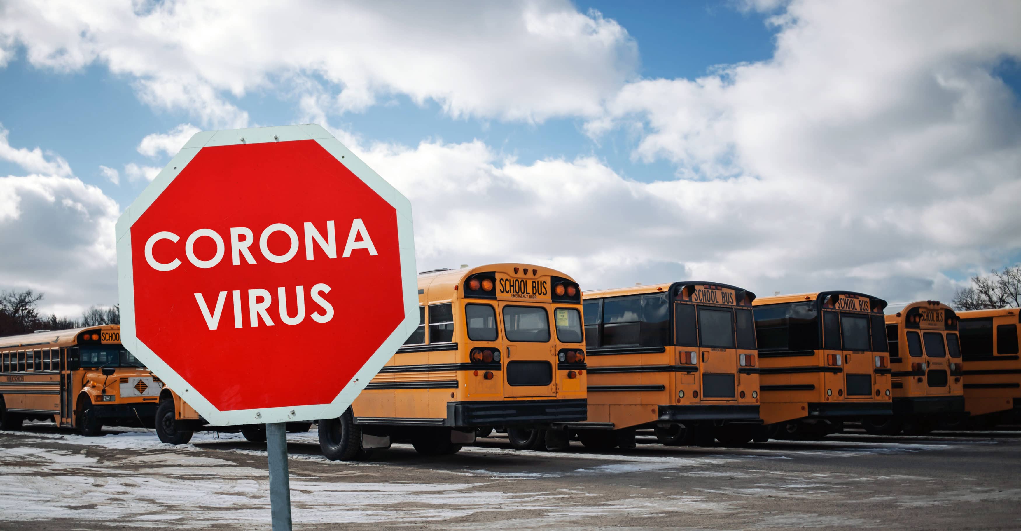 Red sign warning of coronavirus on a background of yellow school bus parking lot. Concept for closing schools or universities for quarantine because of covid-19 epidemic or pandemic outbreak