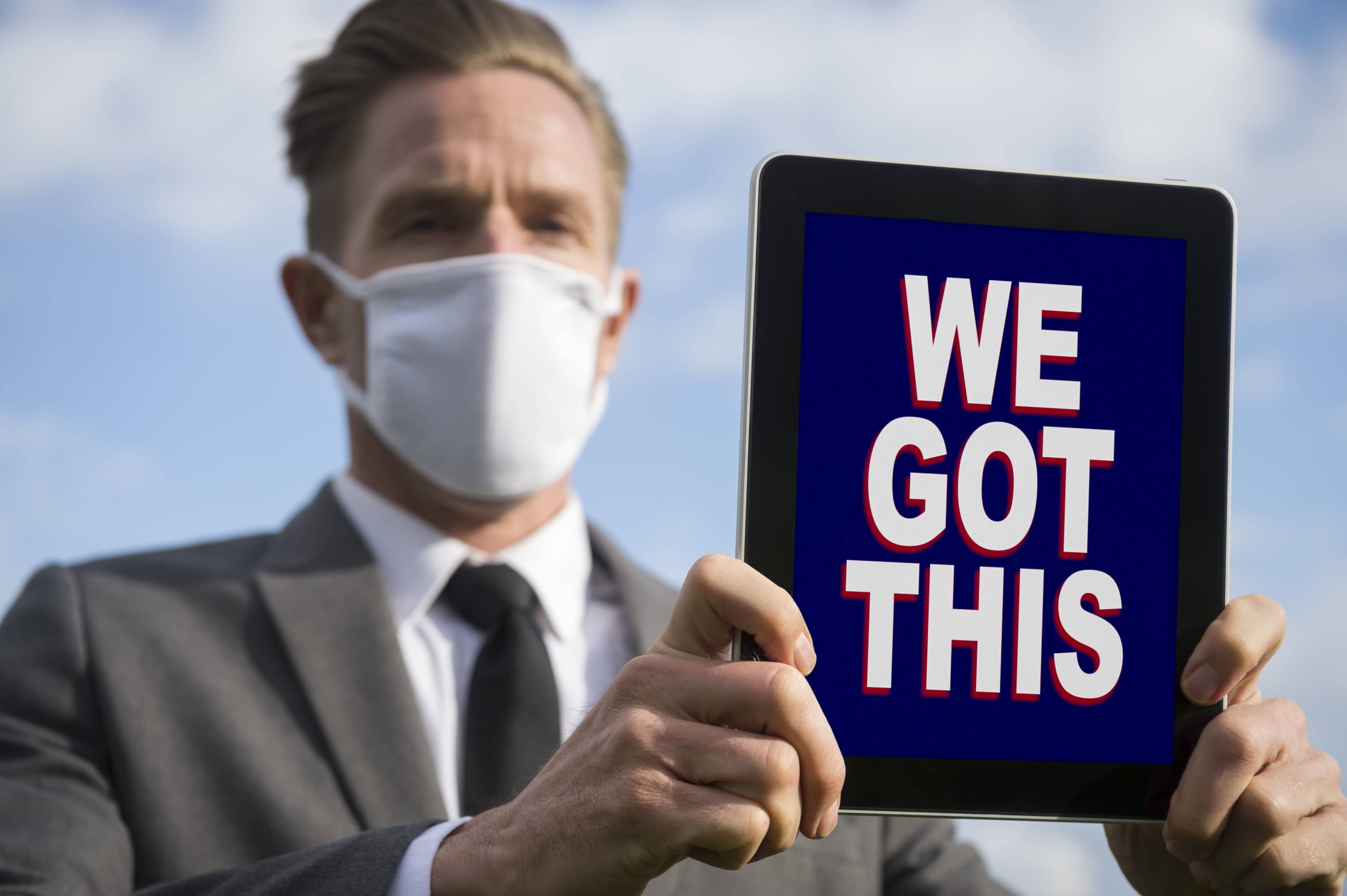 Businessman wearing coronavirus protective surgical face mask holding a tablet with a motivational We Got This message