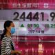 People wearing face masks walk past a bank electronic board showing the Hong Kong share index at Hong Kong Stock Exchange Monday, April 20, 2020. Shares were mixed in Asia on Monday, while oil prices have fallen back. (AP Photo/Vincent Yu)