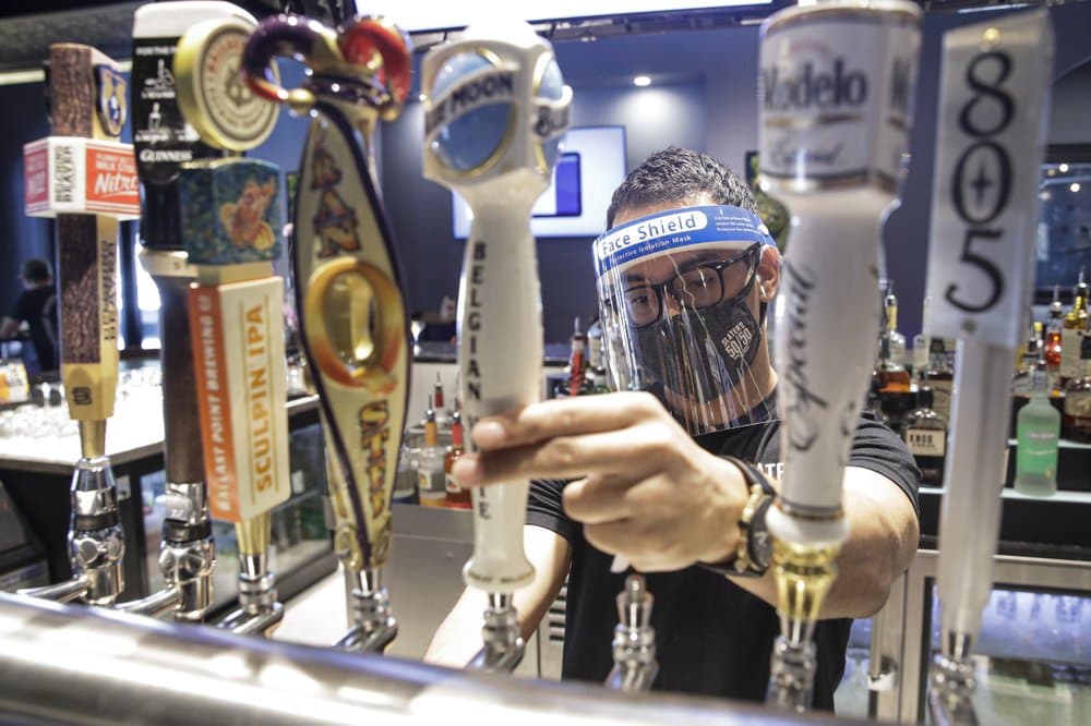 A bartender pours a beer while wearing a mask and face shield amid the coronavirus pandemic at Slater's in Santa Clarita, Calif. California