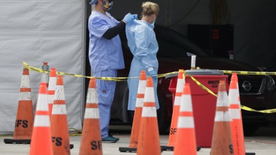 FILE - In this July 5, 2020, file photo, healthcare workers help each other with their personal protective equipment at a drive-thru coronavirus testing site outside Hard Rock Stadium in Miami Gardens, Fla. The PPE that was in dangerously short supply during the initial weeks of the coronavirus crisis in the U.S. is running out again as the virus resumes its rapid spread and the number of hospitalized patients climbs. (AP Photo/Wilfredo Lee, File)