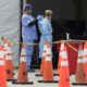 FILE - In this July 5, 2020, file photo, healthcare workers help each other with their personal protective equipment at a drive-thru coronavirus testing site outside Hard Rock Stadium in Miami Gardens, Fla. The PPE that was in dangerously short supply during the initial weeks of the coronavirus crisis in the U.S. is running out again as the virus resumes its rapid spread and the number of hospitalized patients climbs. (AP Photo/Wilfredo Lee, File)