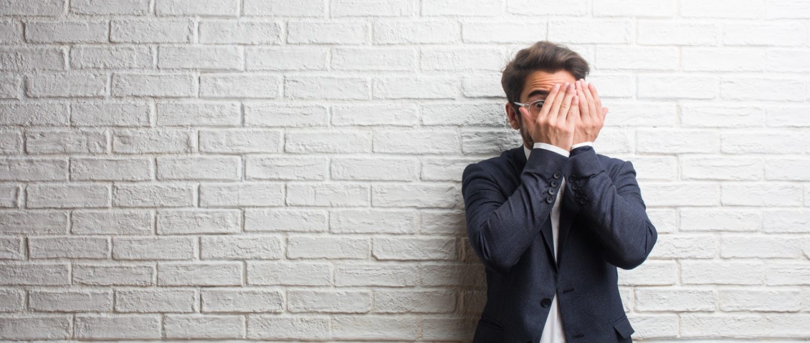 Young friendly business man feels worried and scared, looking and covering face, concept of fear and anxiety