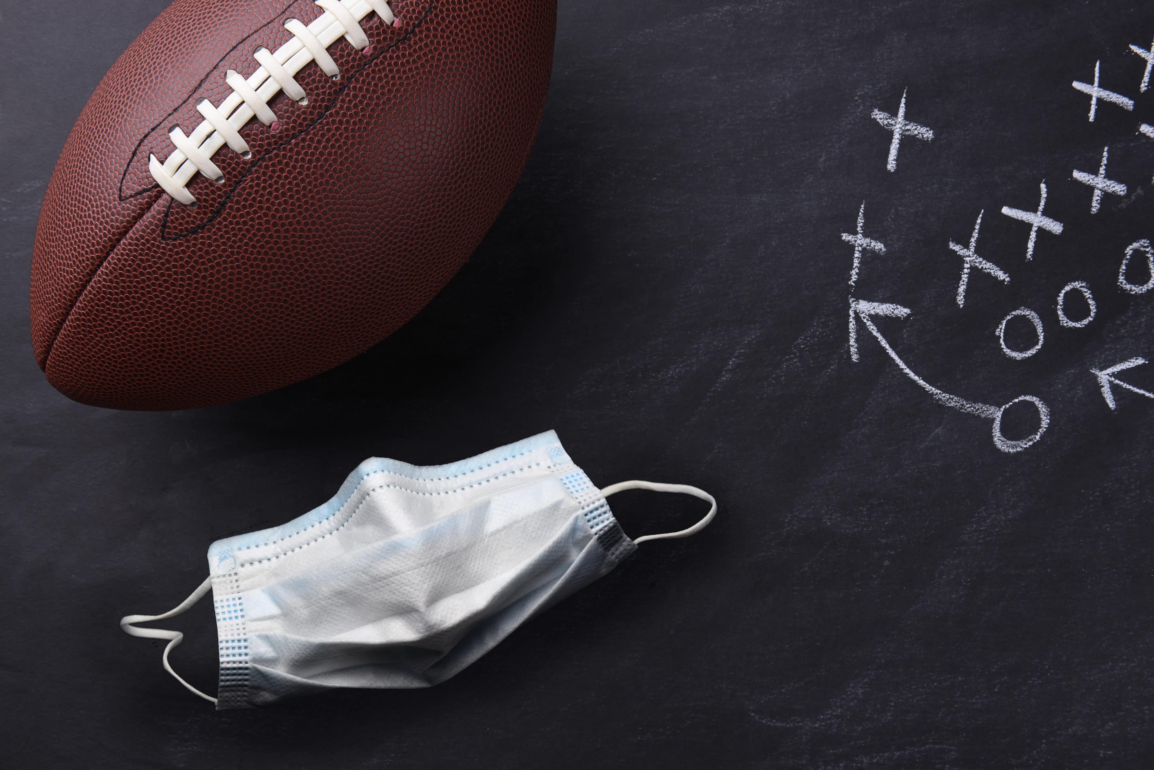 Covid-19 surgical mask and an American style football on a chalkboard with a play diagramed.