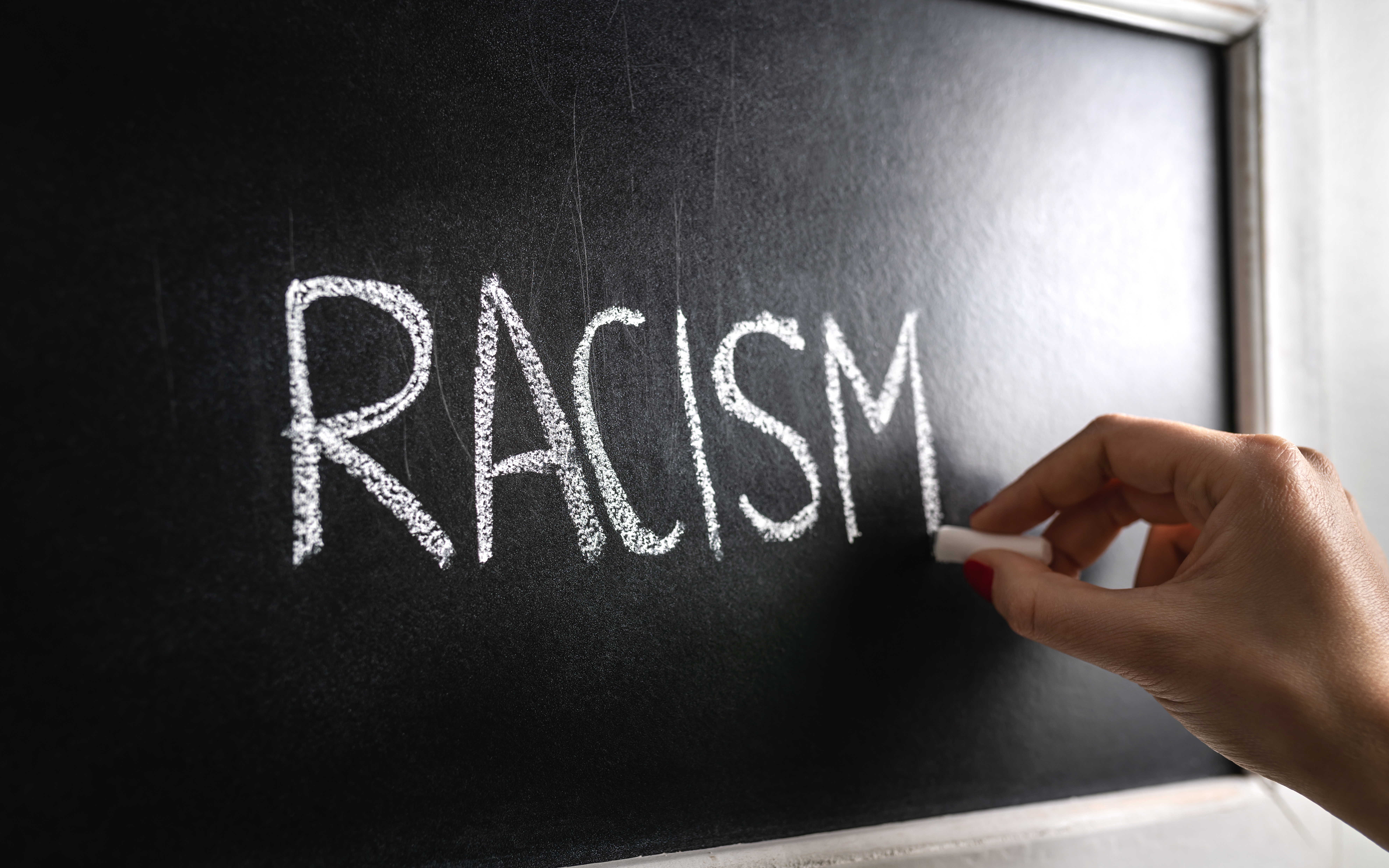 Hand writing the word racism on blackboard. Stop hate. Against prejudice and violence. Lecture about discrimination or stereotypes in school.