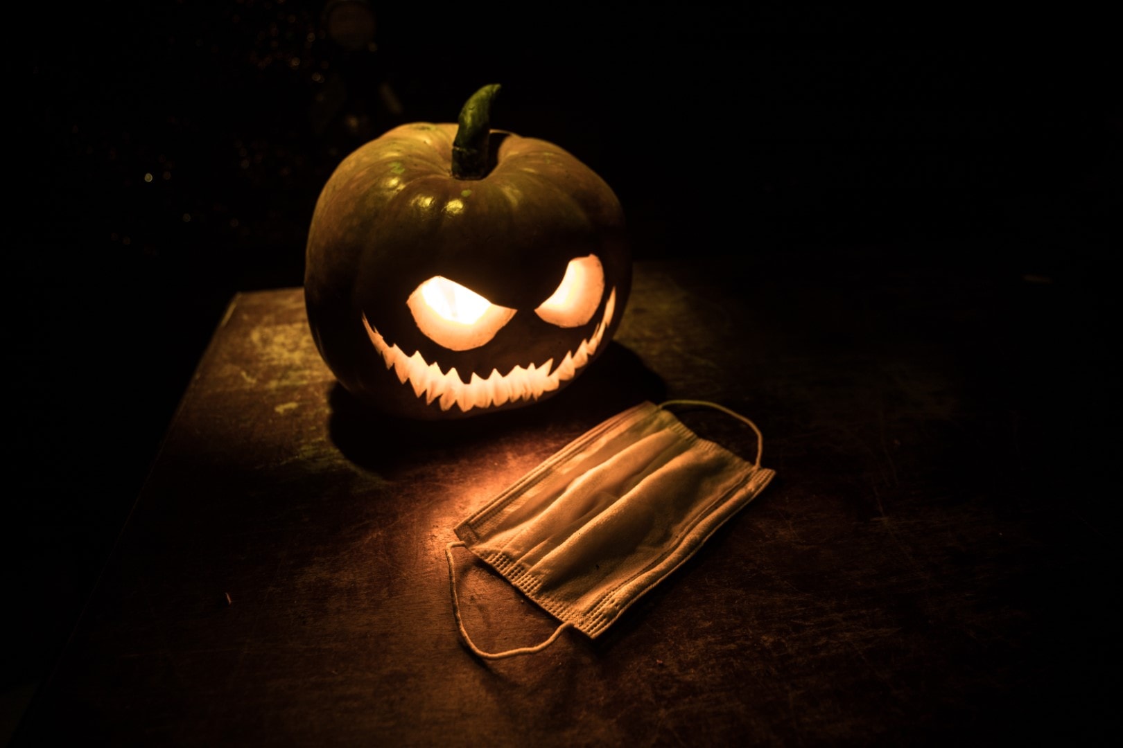 Halloween during Corona virus global pandemic concept. Glowing pumpkins and Covid novel on dark with thematic spooky decorations. Halloween pumpkin on foggy backlight.