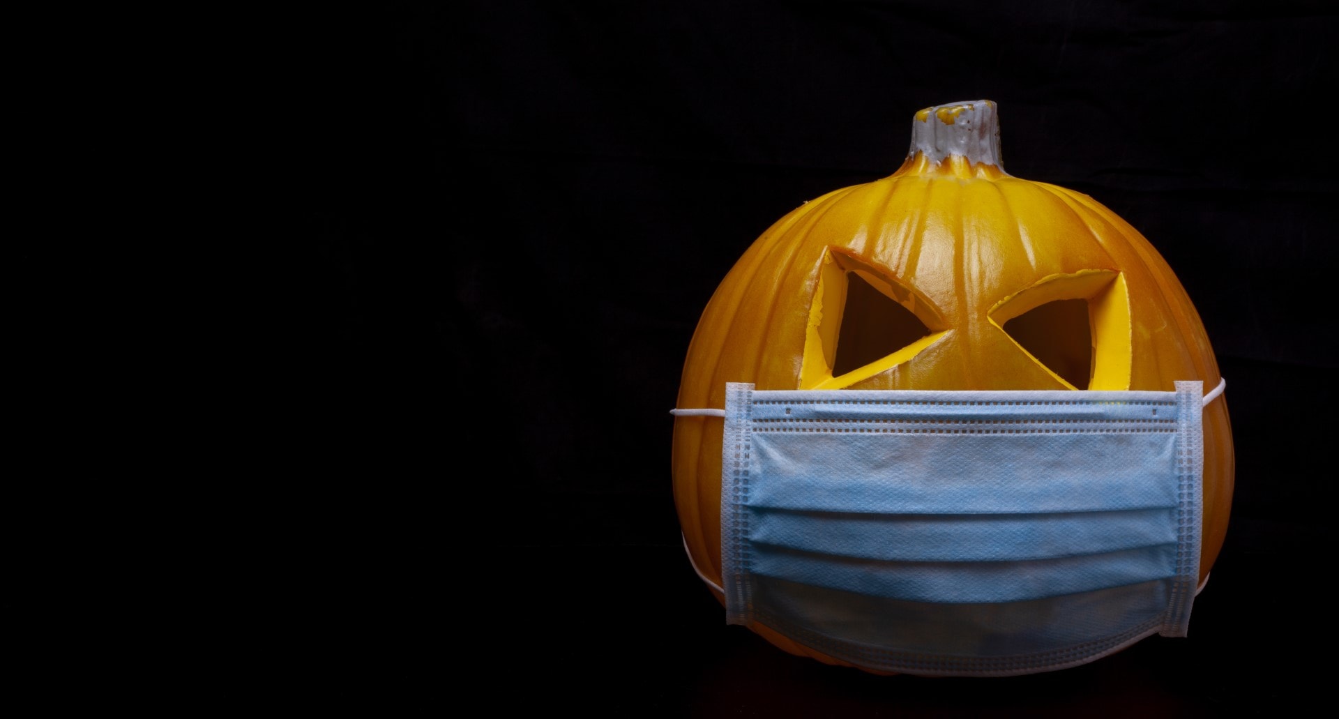 halloween in the age of coronavirus - pumpkin with face mask on black background