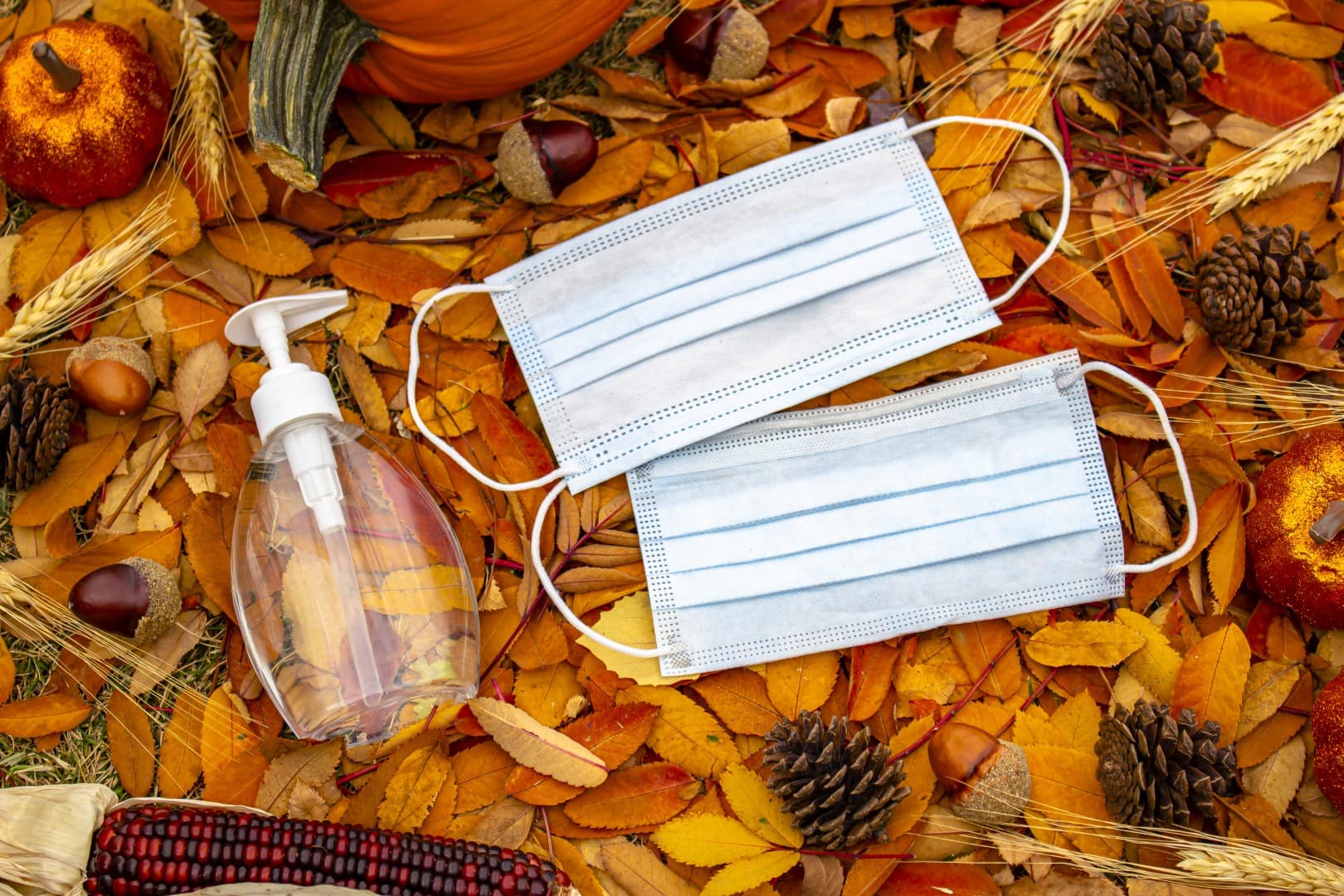 A bottle of a hand sanitizer and face mask on a halloween and thanksgiving background. Concept: Halloween and Thanksgiving during a pandemic, covid-19, coronavirus.