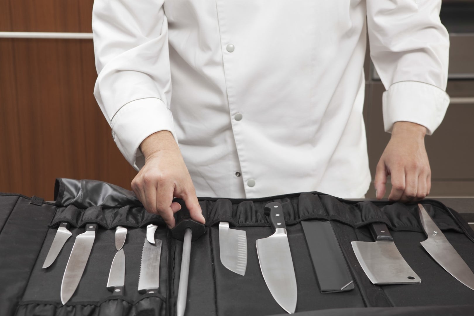 Midsection of male chef selecting knife sharpener out of full set in commercial kitchen