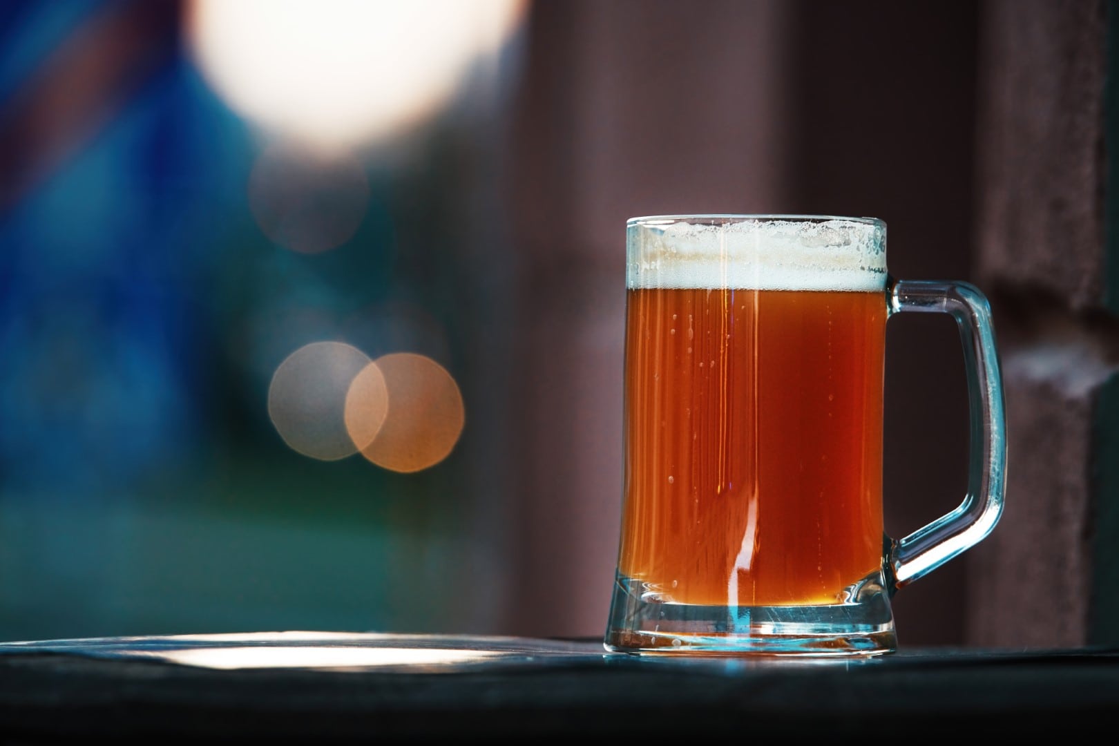Cold beer mug with foam at sunset. Beer glass of red ale. Glass of dark beer standing on the bar of summer terrace seducing people to go to the pub and try foamy alcoholic drink, street background