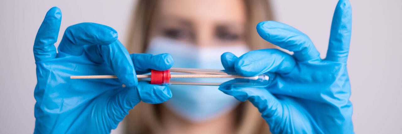 Nurse with facem ask holding Coronavirus COVID-19 swab test kit, PPE protective mask and gloves, tube for taking OP NP patient specimen sample, PCR DNA RNA testing protocol process