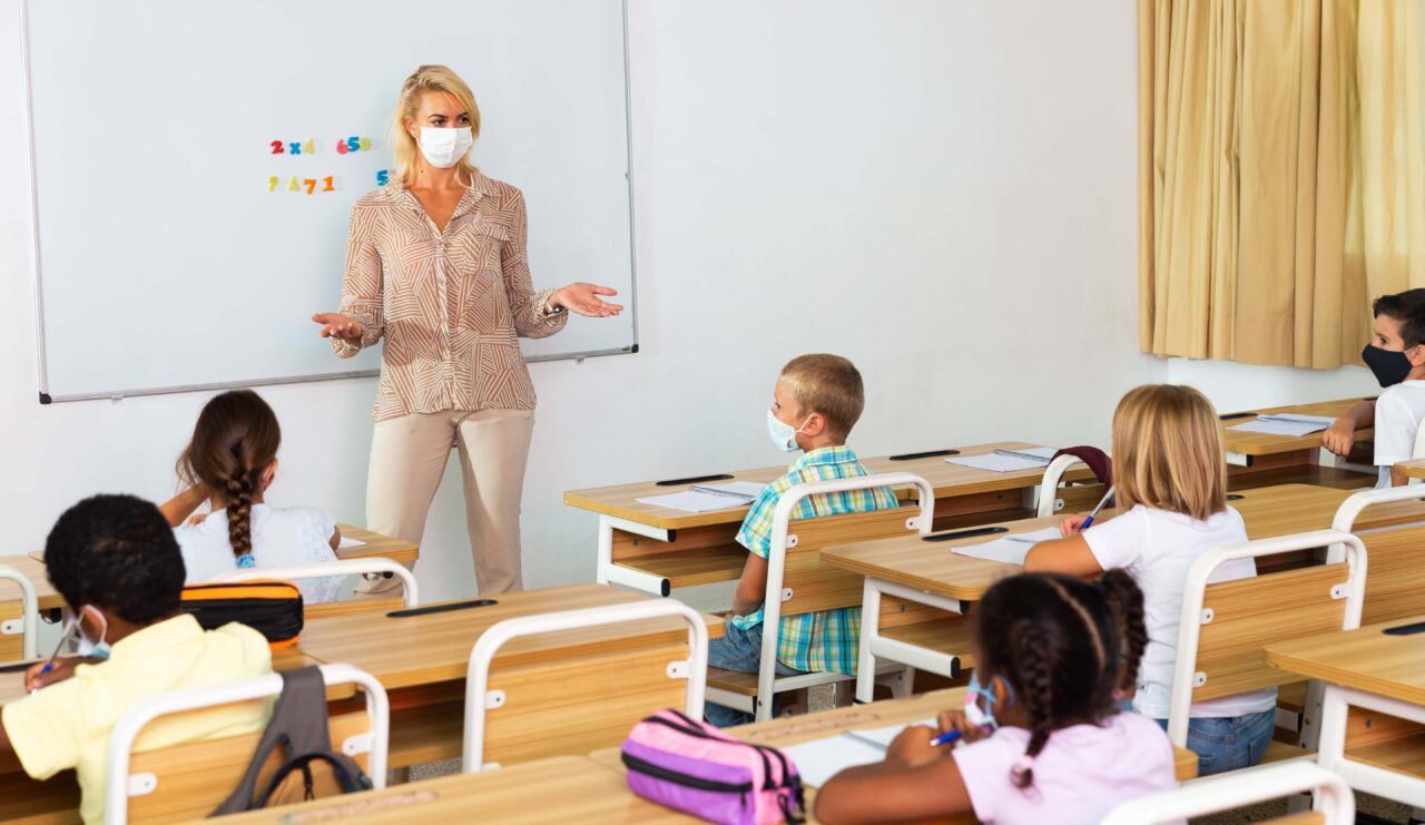 Female teacher in protective mask giving lesson to children