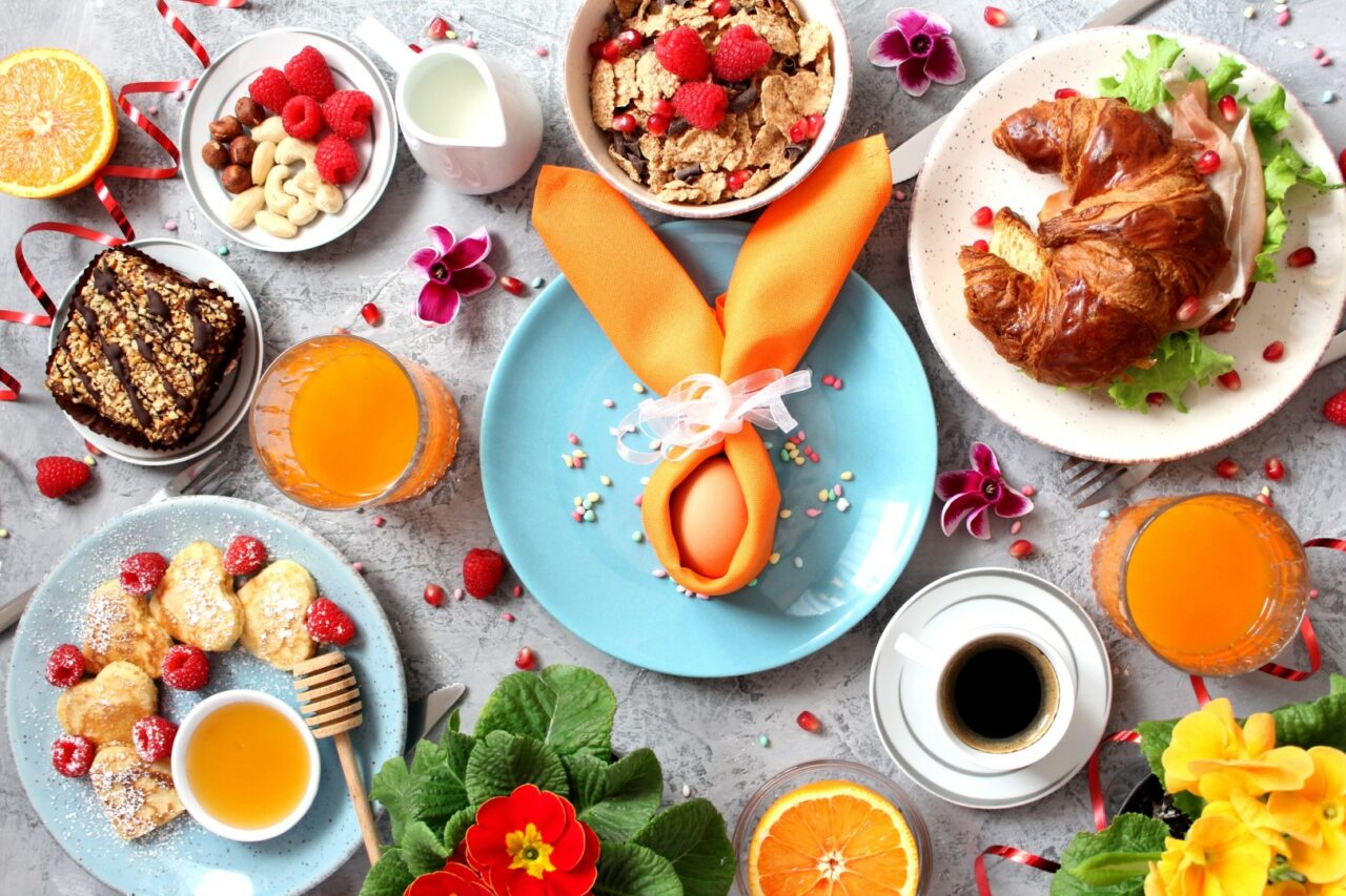 Breakfast food table. Festive brunch set, meal variety with pancakes, croissants, juice, fresh berries, granola and fresh fruits. Easter breakfast. Top view with copy space.