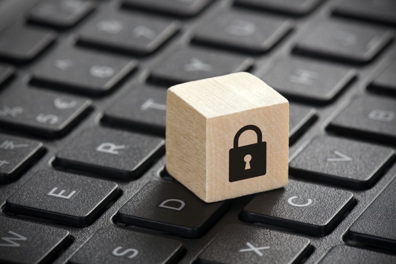 Wooden block with lock graphic on laptop keyboard. Computer security concept.