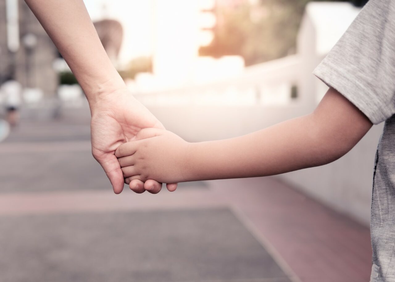 A parent holds the hand of a small boy in the sunset.