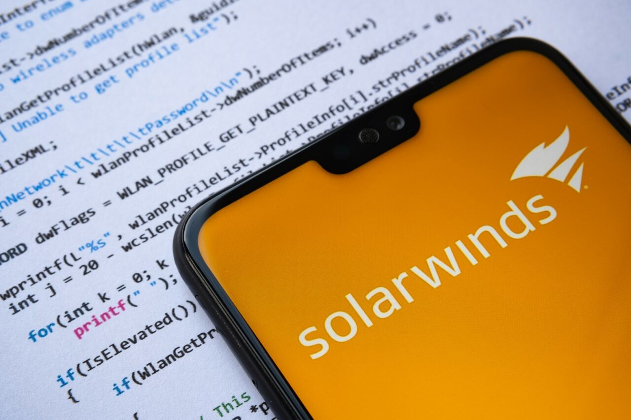 Stafford, United Kingdom - January 2 2021: Solarwinds logo seen on the smartphone screen, with simple C attack code on the paper background.