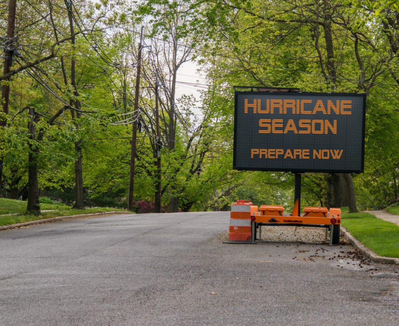 Digital electronic mobile road sign that says Hurricane Season prepare now, on the side of a tree lined road