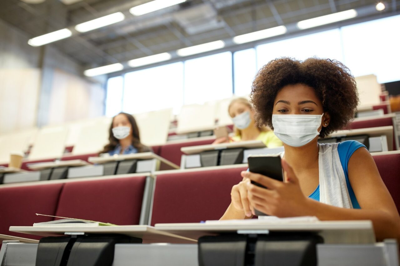 student girl in mask with smartphone at lecture