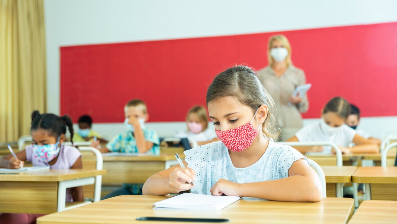 Diligent tween girl in protective mask studying in school