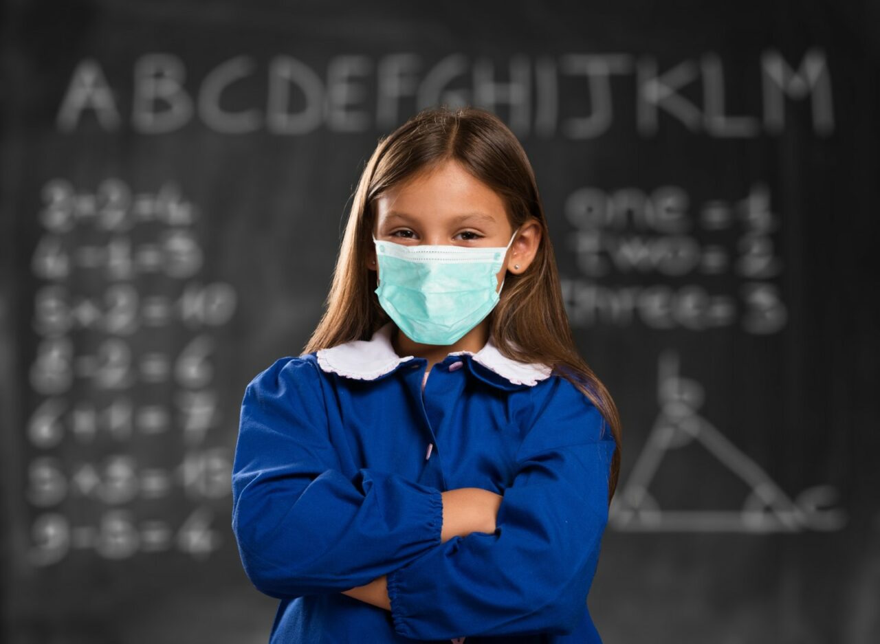 Masked girl at school in front of a blackboard
