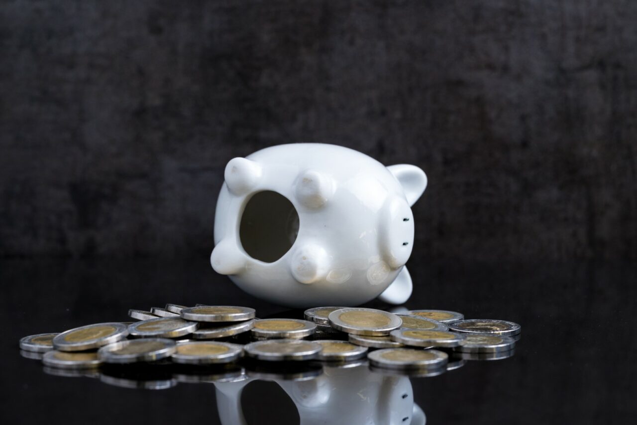 Empty piggy bank lay on dark black table with coins using as broke or personal finance problem crisis
