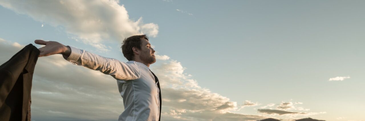 Businessman embracing life standing under cloudy sky