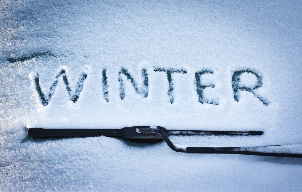 Winter written in snow on car windscreen below windscreen wiper