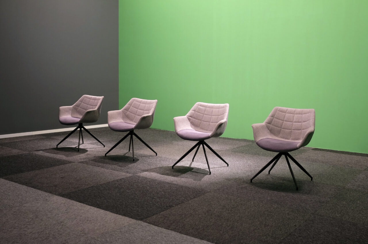 Four empty chairs in a TV studio with green screen background