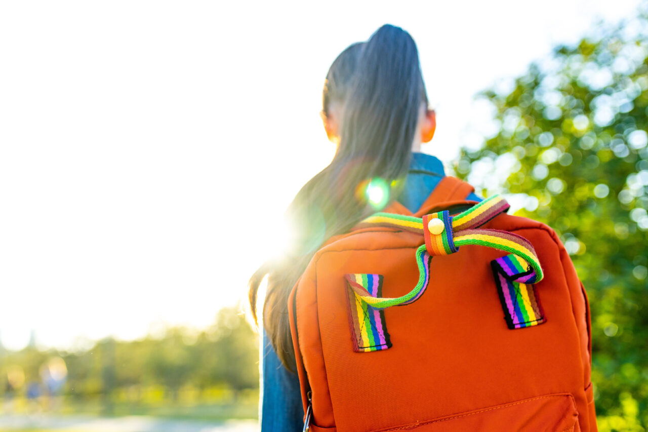 girl student wears backpack outdoors in summer park