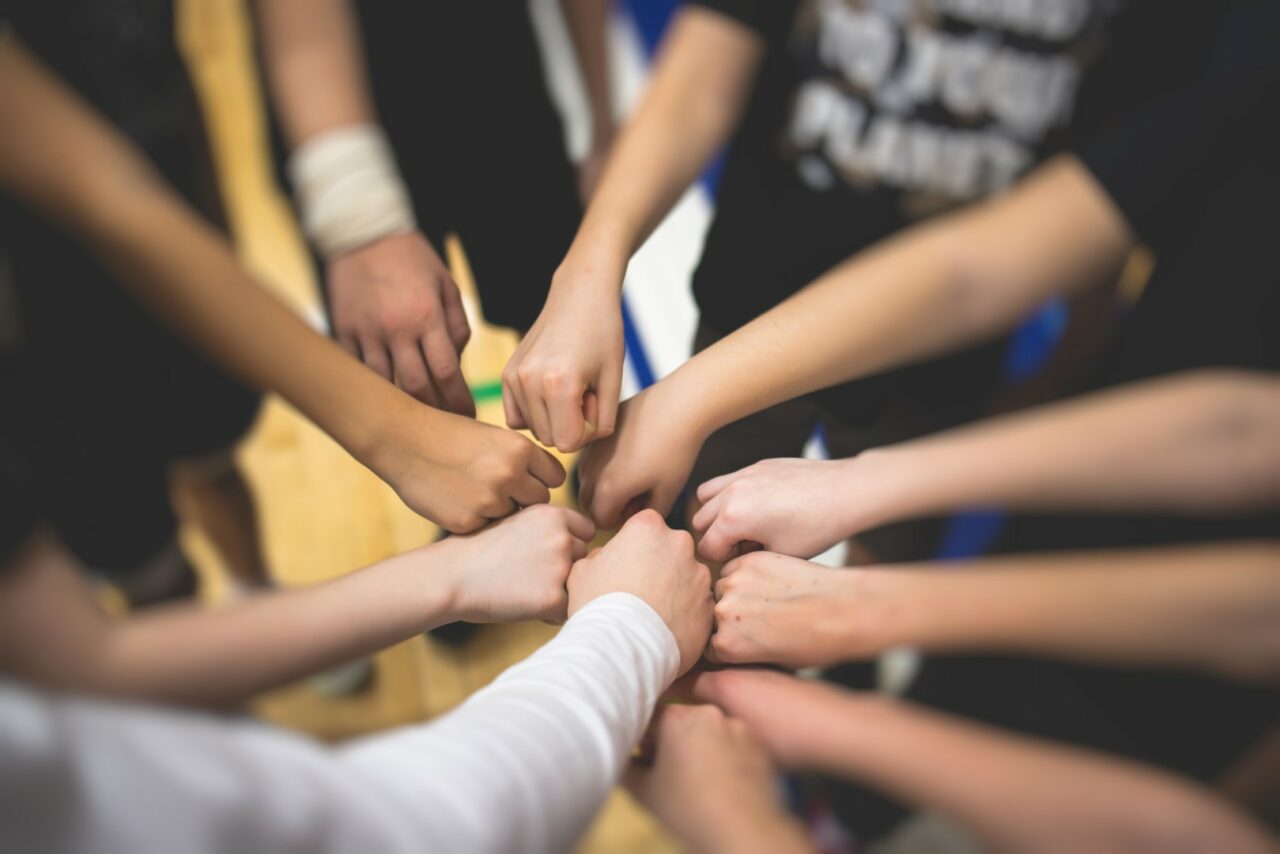 Team of kids children basketball players stacking hands in the court, sports team together holding hands getting ready for the game, playing indoor basketball, team talk with coach, close up of hands