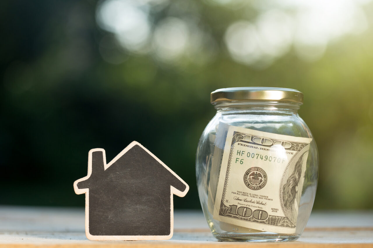 Real estate concept - money jar and little house with space for text on the wooden table in the garden