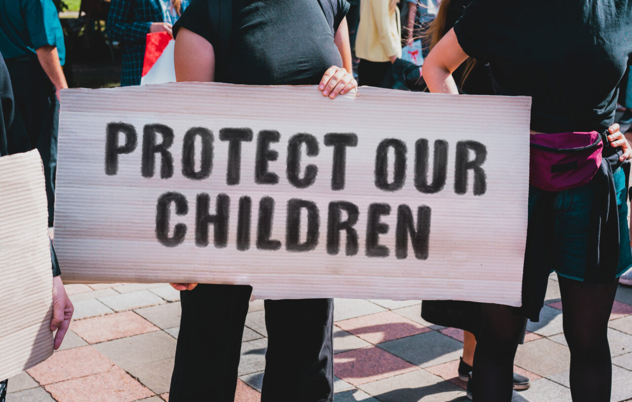 The phrase " Protect our children " drawn on a carton banner in