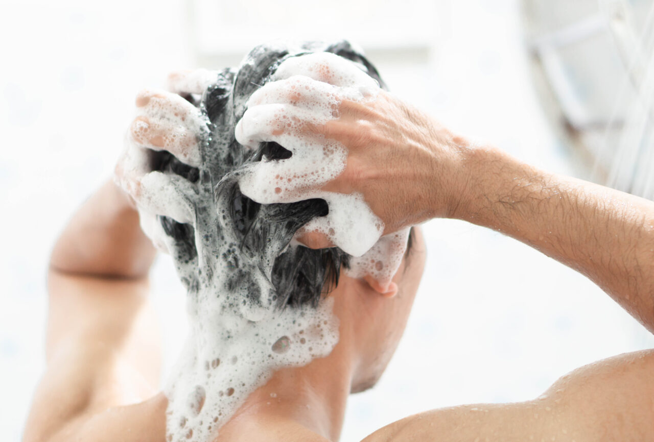 Closeup young man washing hair with with shampoo in the bathroom