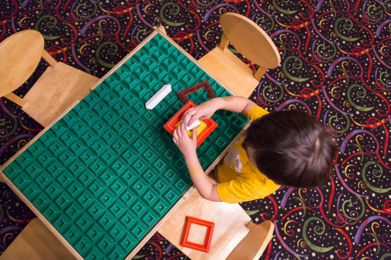 Overhead of Mixed-race Boy Sitting at a Work Table Playing with Building Blocks Toys.