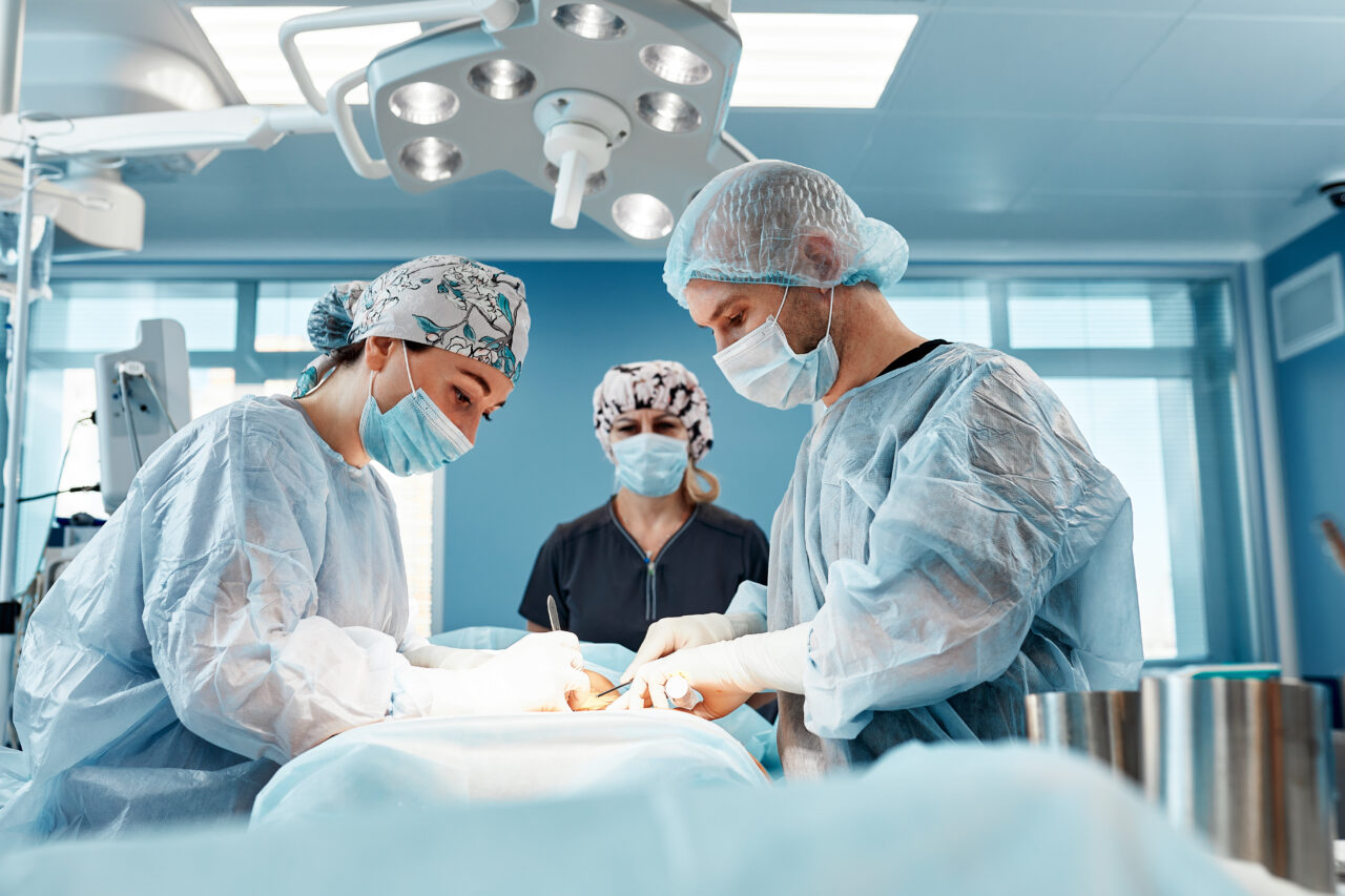 Doctors performing abdominoplasty surgery in the hospital. Focus on male plastic surgeon doing abdominal plastic surgery in operating room. Concept of tummy tuck and cosmetic surgery.