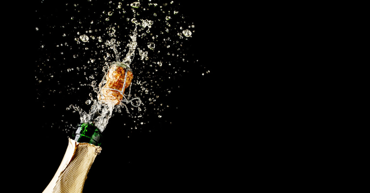 Champagne cork popping and splashing on black background