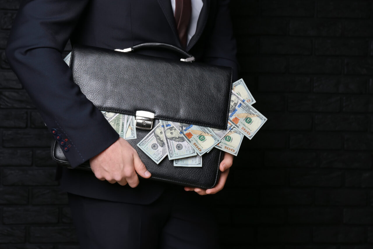 Businessman holding briefcase with dollar banknotes on dark back